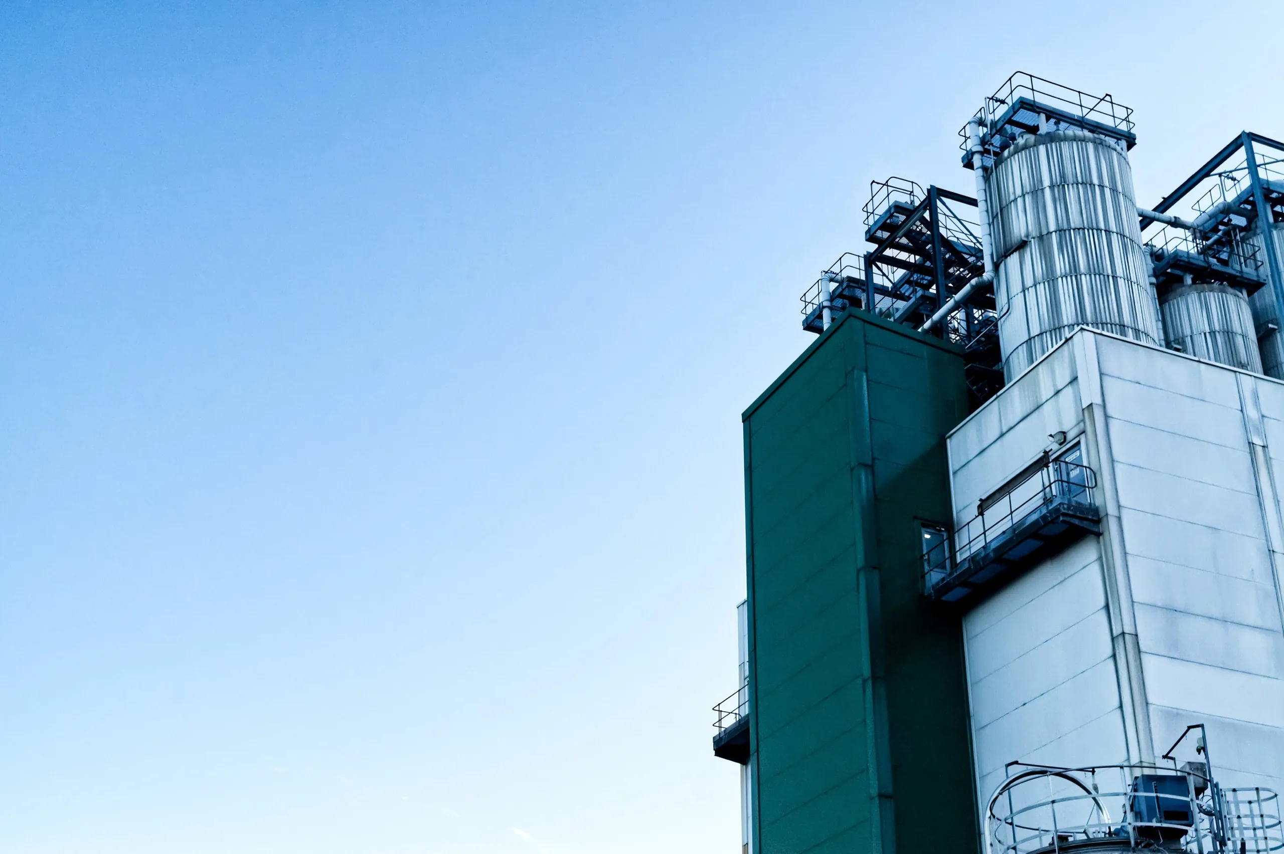 Steel silos and the green service tower of a process plant against a clear sky
